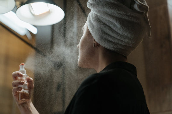 Woman sprays freshener on face